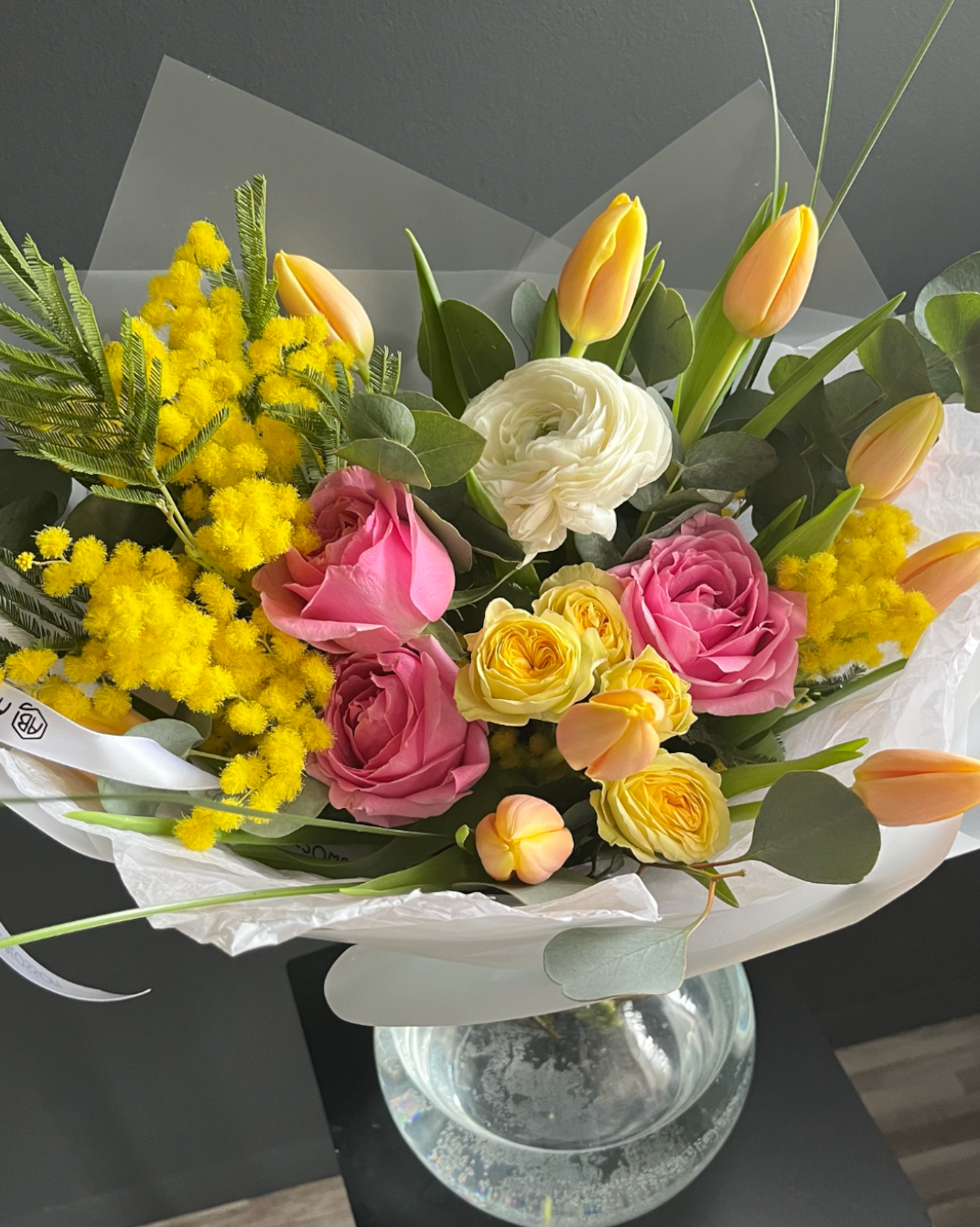 Floral arrangement with yellow, pink, and white flowers on a glass stand in photo editing software.